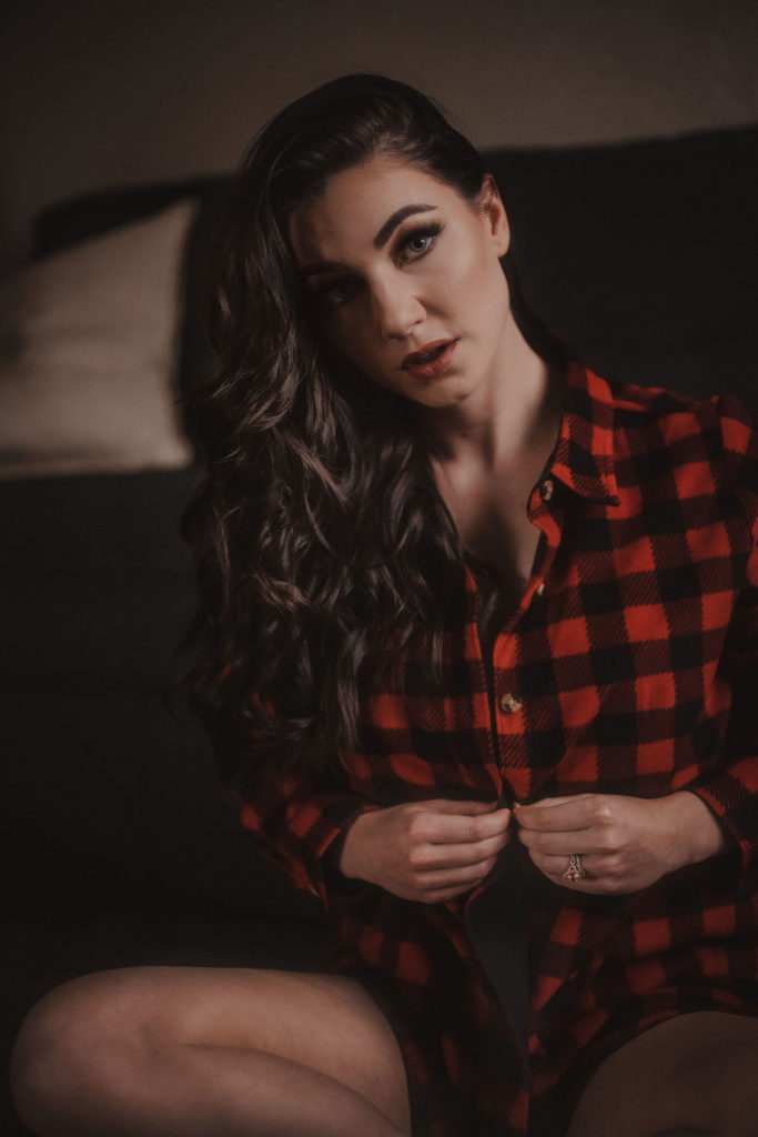 A beautiful woman unbuttoning her red checkered shirt while looking at the camera