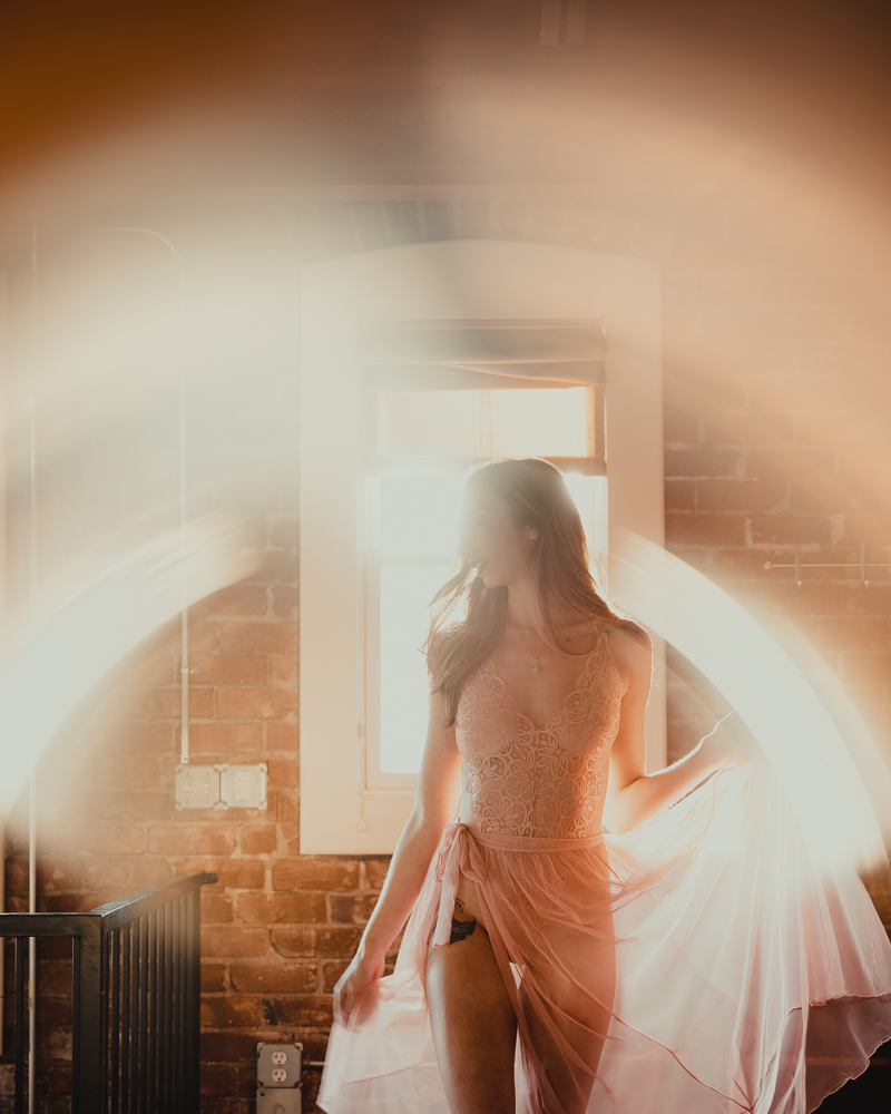 A unique photography idea using sun flare wrapped around a woman in pink lingerie dress that is artistically lit.