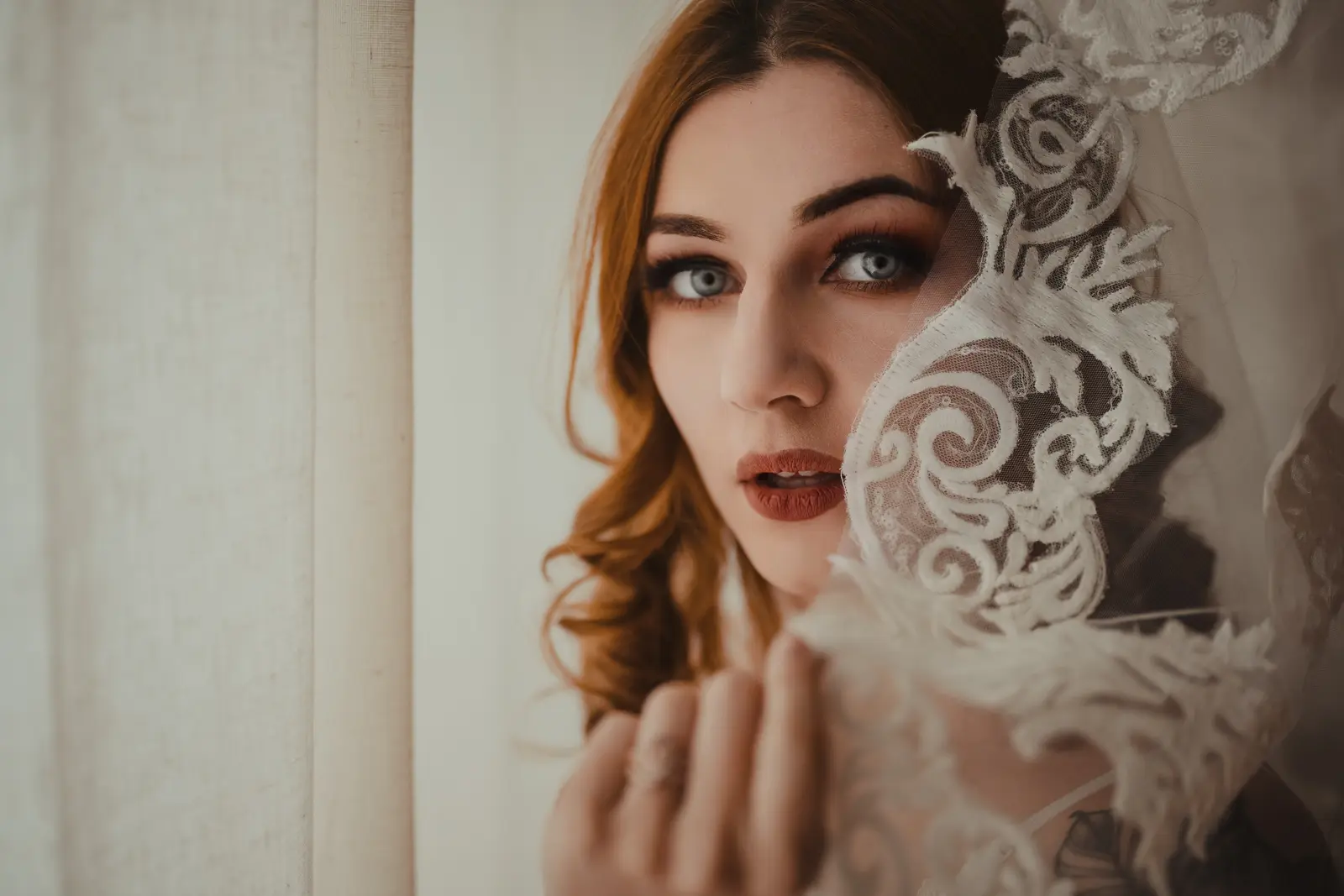 A bride with blue eyes looking at the boudoir photographer with her wedding dress next to her. The photo has a moody edit with rich tones